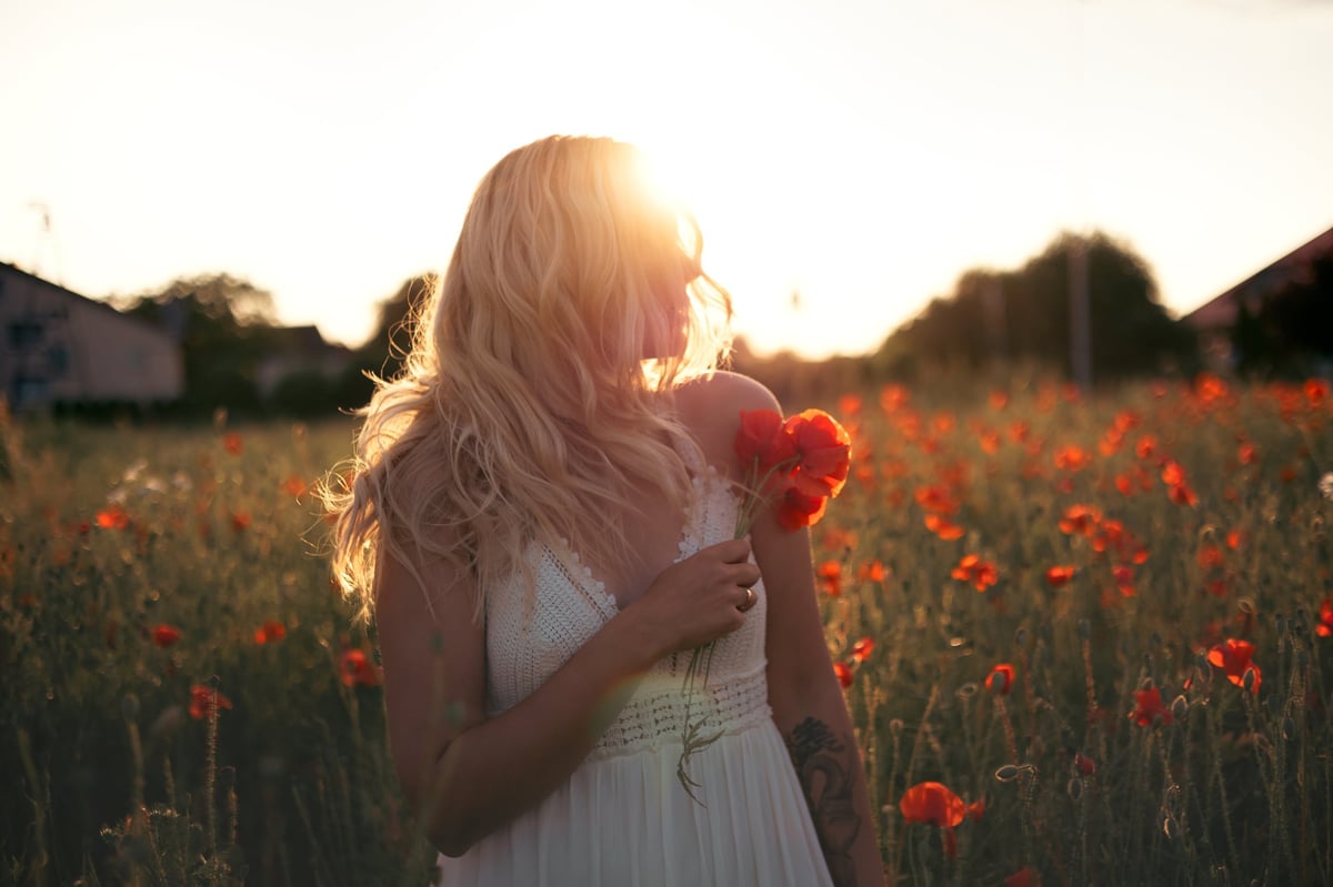 Young beautiful blonde woman in white dress in poppy field at sunset