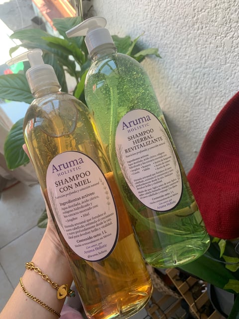 Two Aruma branded shampoo bottles - one honey shampoo and one revitalizing shampoo - held in front of a potted plant
